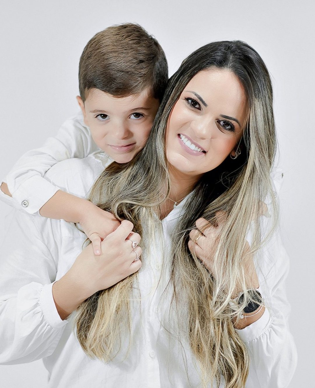 A Aninha sorrindo, abraçada pelo filho Apolo
